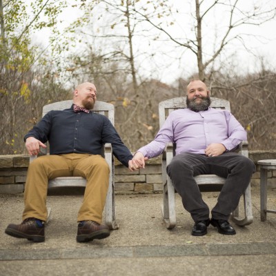 Two men holding hands sitting in Adirondack style chairs - michigan gay engagement photographer