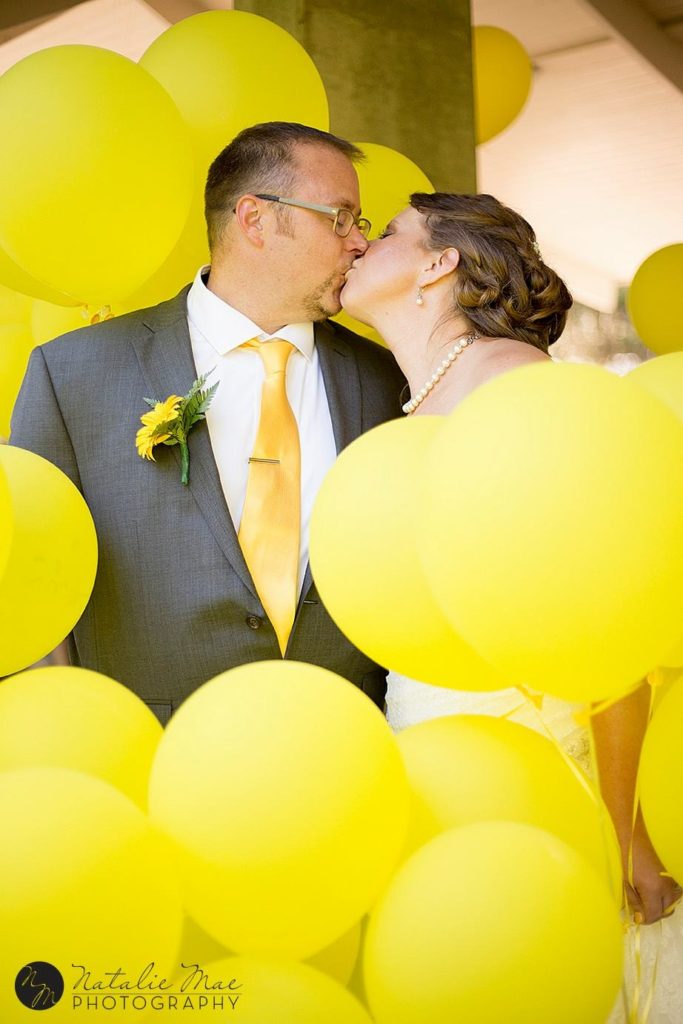 Island Park wedding couple surrounded by yellow balloons kissing.