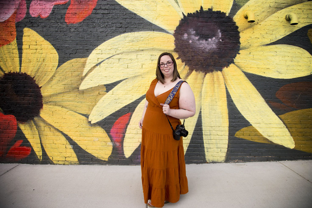 Jackson, Michigan photographer Natalie Jones wearing a burnt orange dress with giant sunflower mural behind her