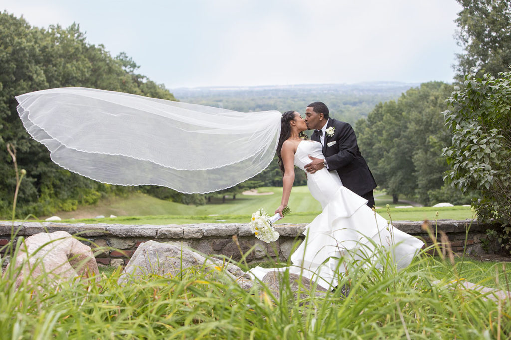 Bride and groom kissing with cathedral length veil blowing in the wind - Spring wedding pose idea