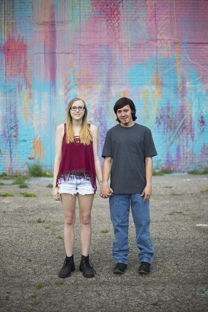 Couple holds hands in front of bright mural