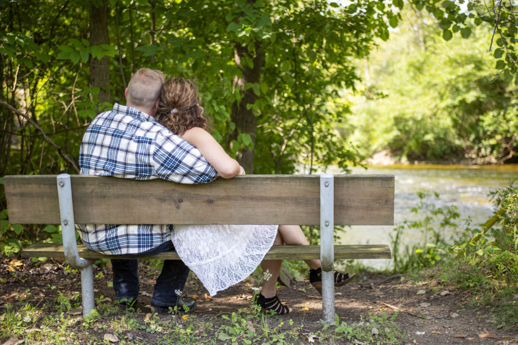 Engaged Michigan couple cuddles on park bench