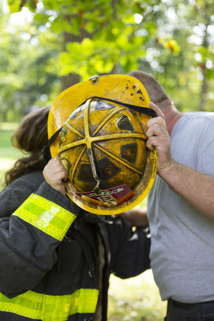 Firefighter and nurse kiss behind fire helmet during their Dexter engagement session