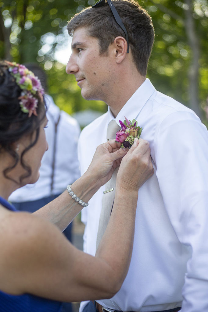 Groom getting boutonnière pinned on by mother