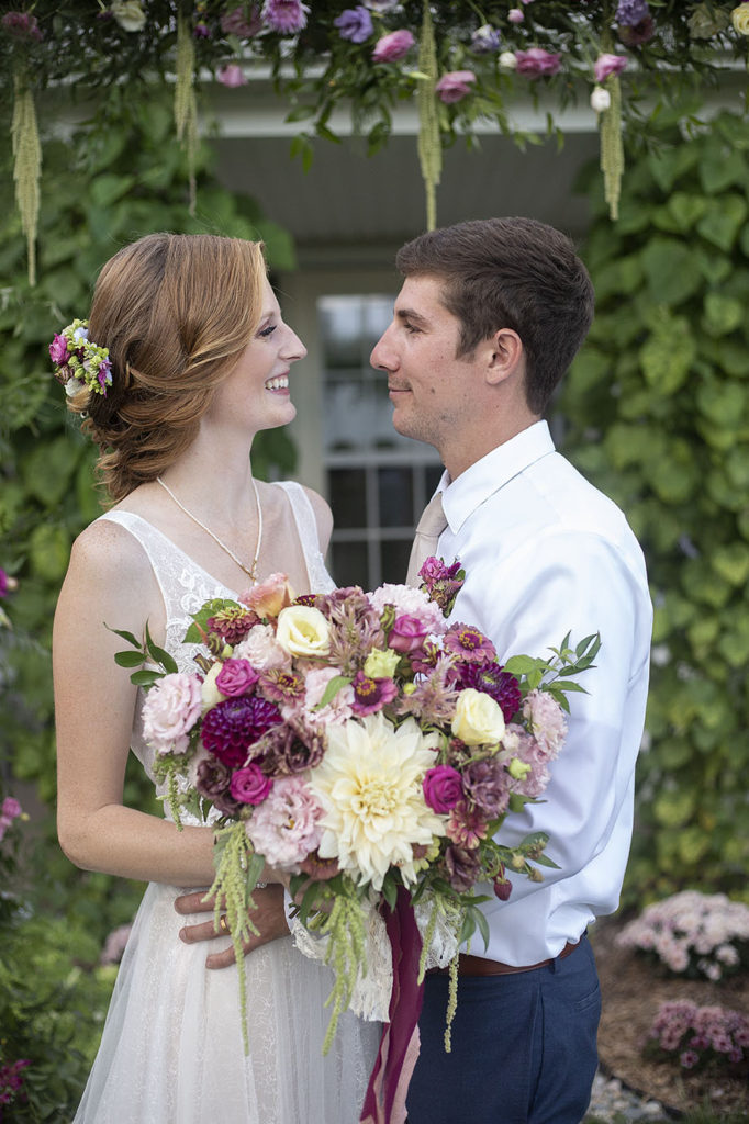 Carmen and Chris looking at each other in front of floral arbor