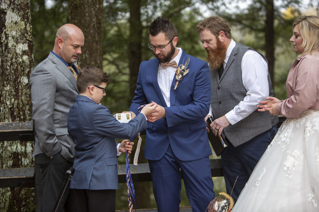 Ring bearer handing off rings and hand fasting rope Tahquamenon Falls elopement