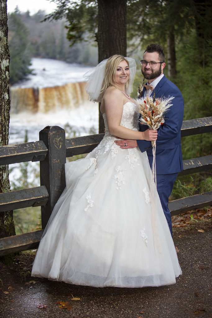 Wedding couple poses in front of Tahquamenon Falls