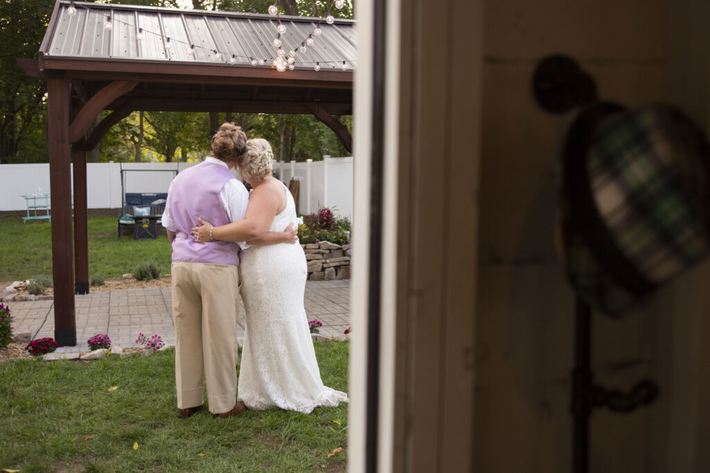 Same sex wedding couple snuggle together while their guests party