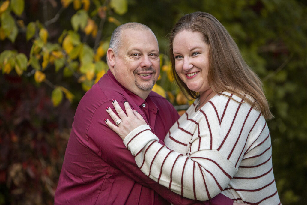 Fire department engagement couple poses in front of fall leaves