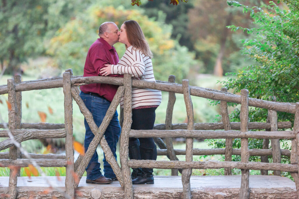 Fire department engagement couple cuddle together on bridge at McCourtie Park in Jackson MI