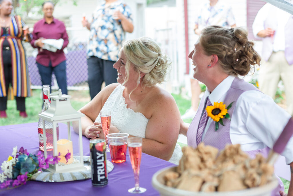 Lesbian couple watching their friend give a toast during their backyard Westland wedding