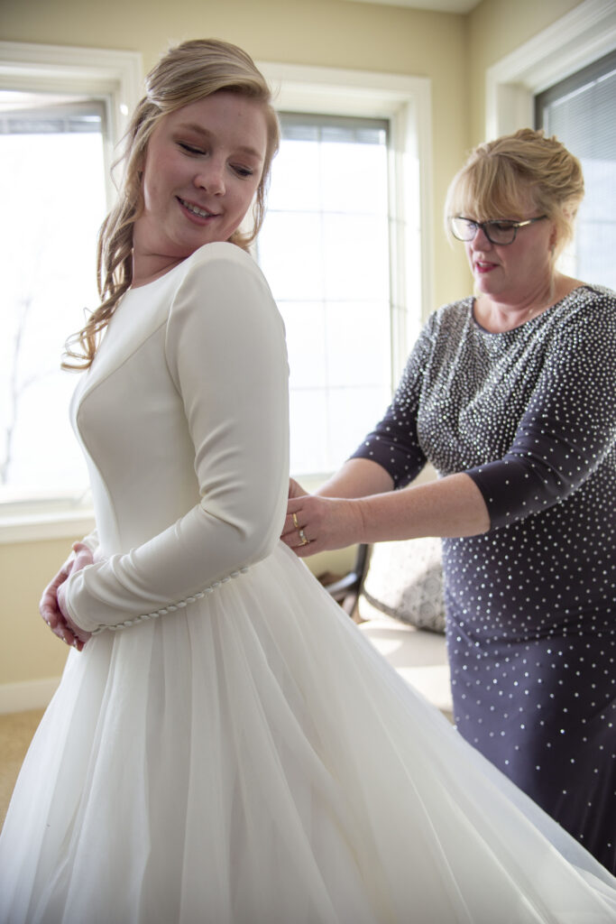 Mom helps bride fasten the back of her dress before her Lake Michigan AirBNB wedding