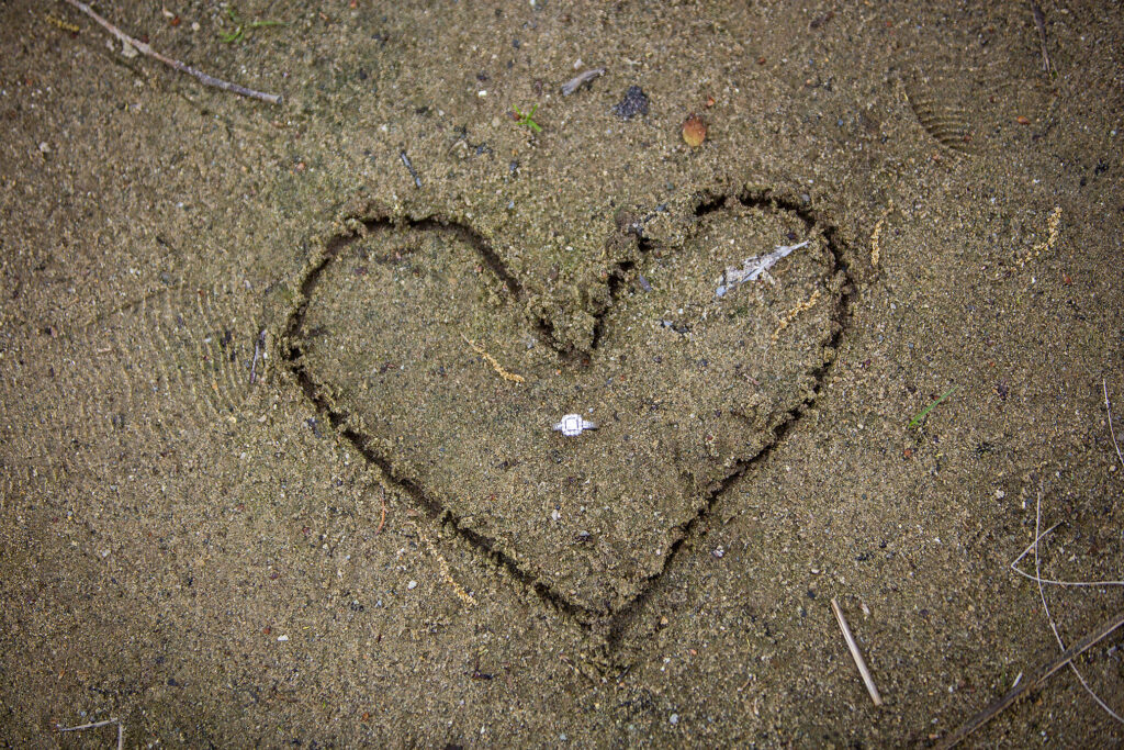 Kensington Metropark engagement ring in the center of a heart drawn in the sand