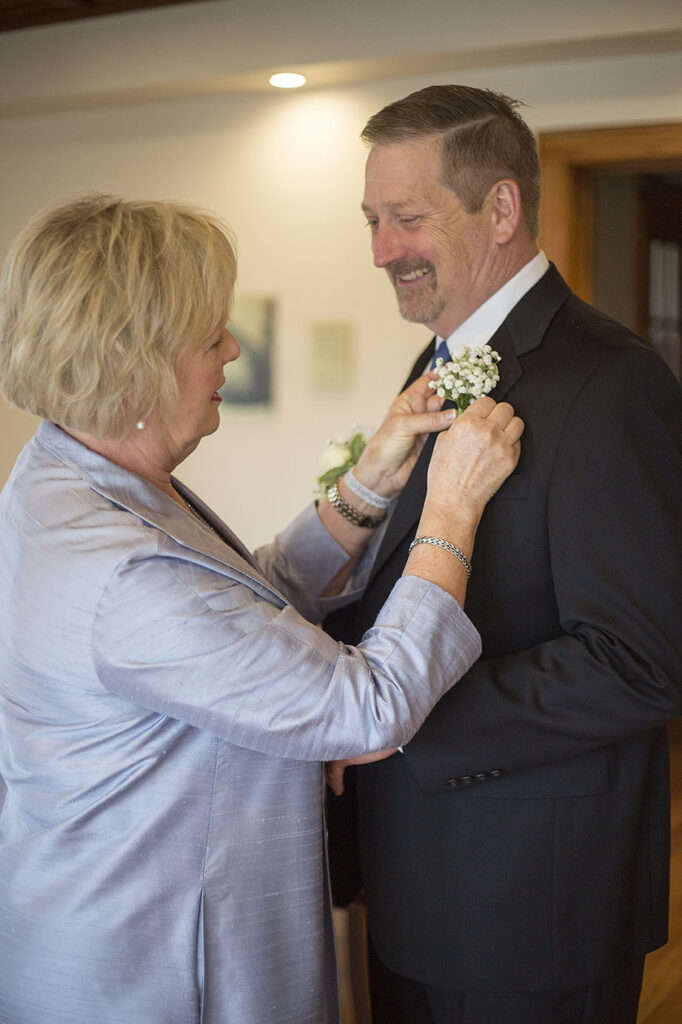 Dad smiling at mom as she pins on boutonniere before Plymouth wedding