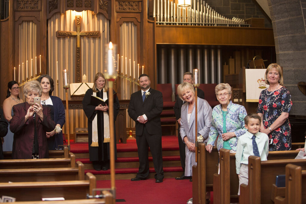 Guests smiling at bride as she walks down the aisle at Plymouth wedding