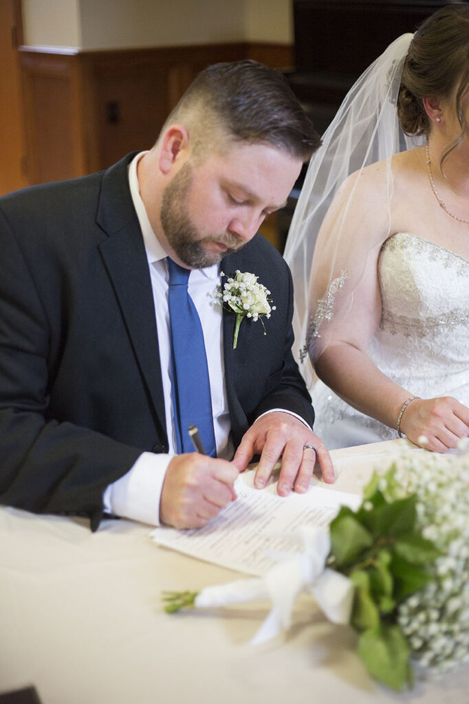 Groom sitting next to bride signing marriage certificate Plymouth wedding