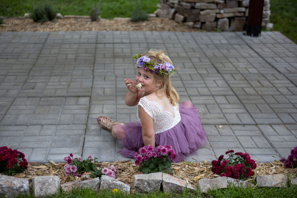 Flower girl sitting on the ground while eating wedding cake at Westland wedding