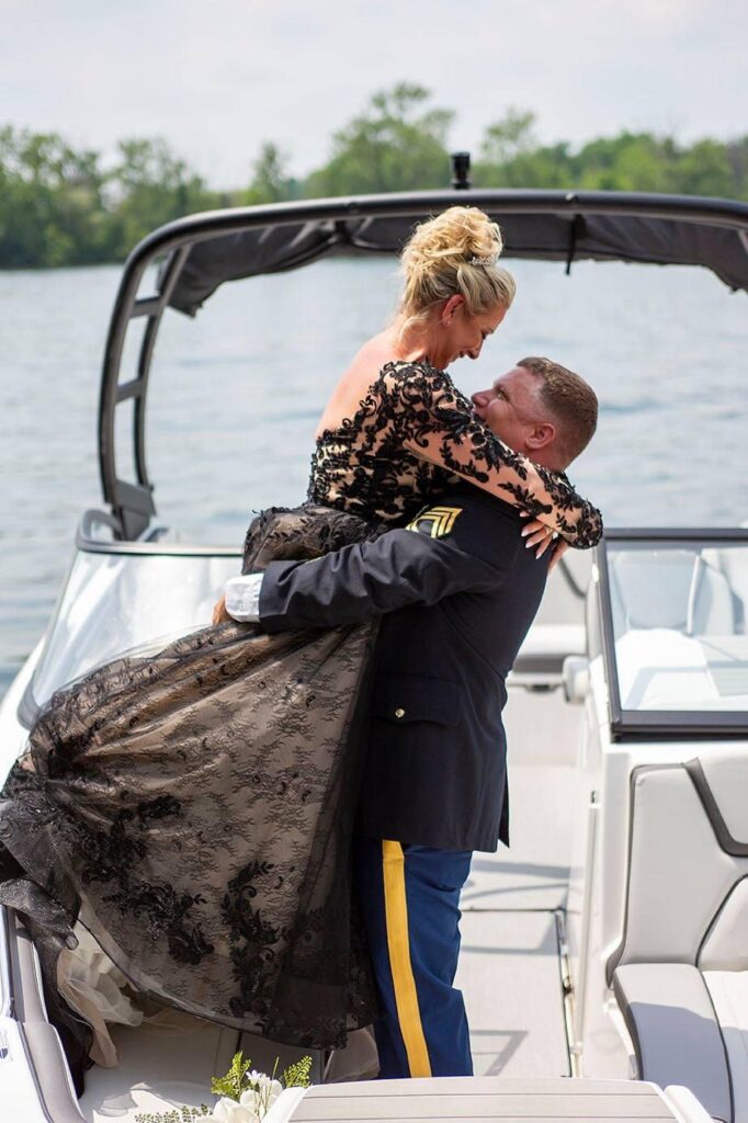 Michigan groom lifts up new bride on their boat in Belleville Lake.