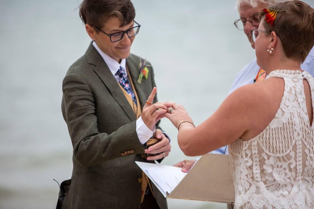 Michigan LGBTQ wedding couple exchanges rings on the beach at the Elk Rapids Day Park.