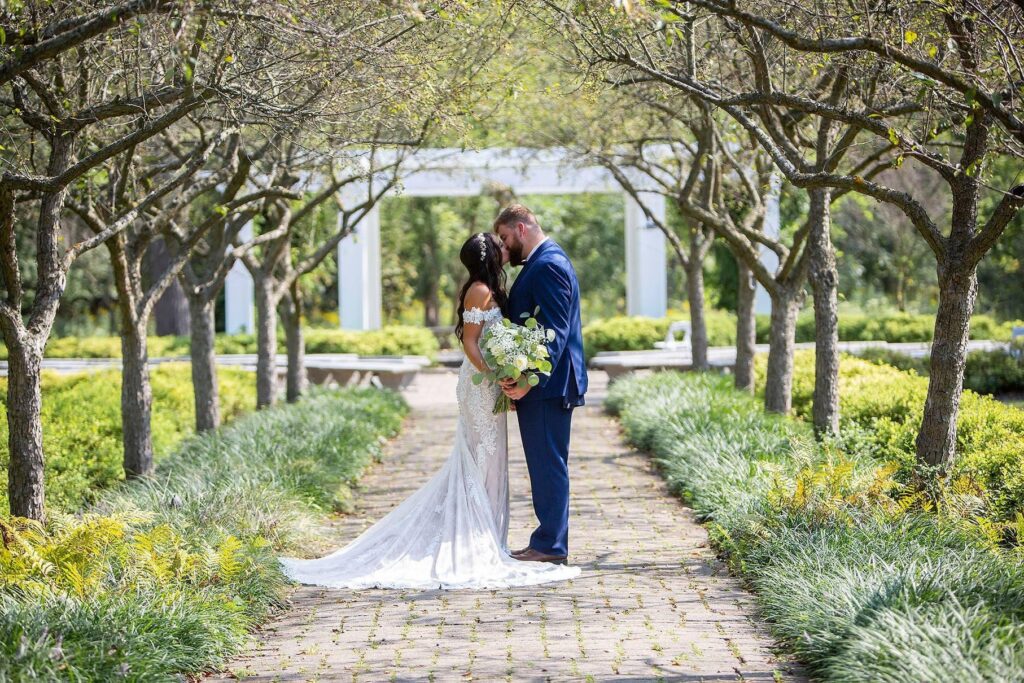 Saline Michigan wedding couple kisses in the middle of a tree lined path at Wellers Carriage House in Saline.