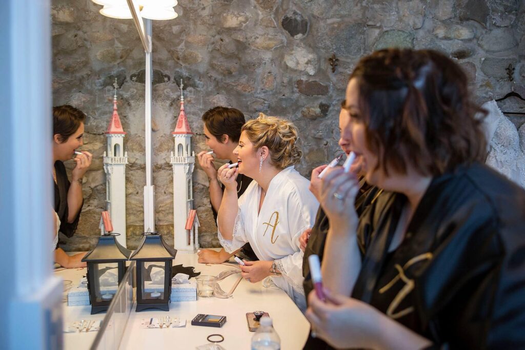 Bride and bridesmaids putting on makeup in a mirror at Castle Farms in Charlevoix.