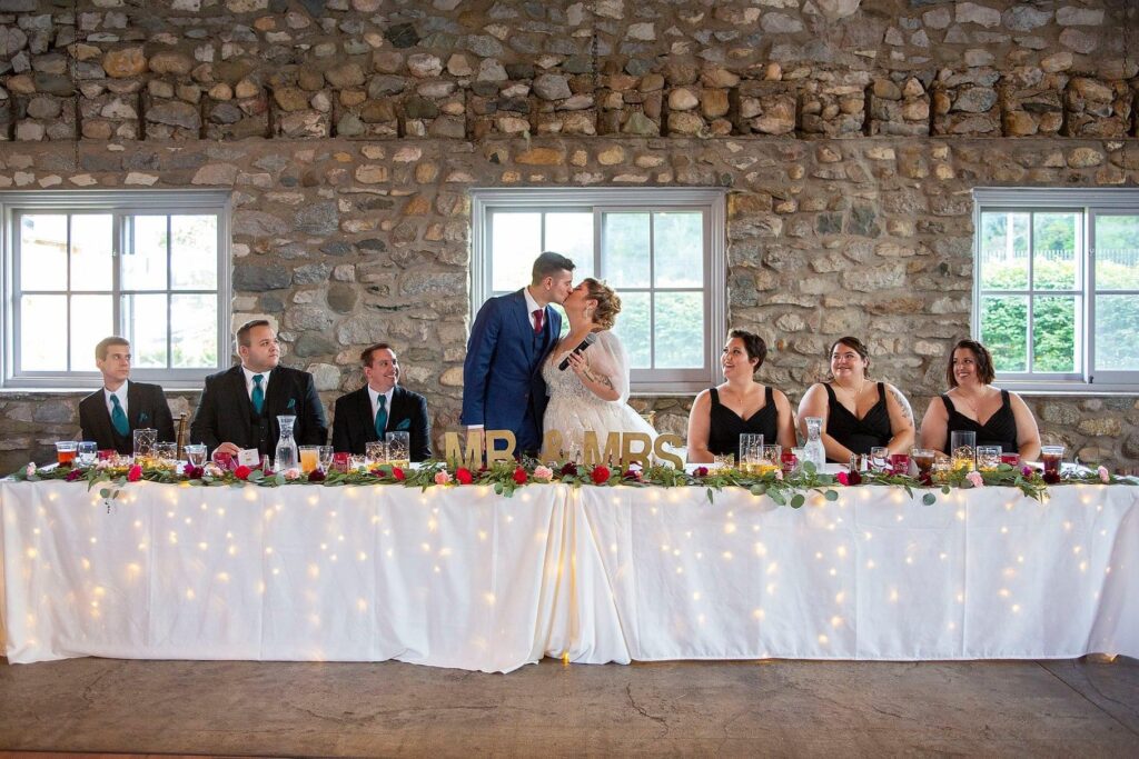 Couple kisses while guests clank their champagne glasses at Charlevoix wedding.