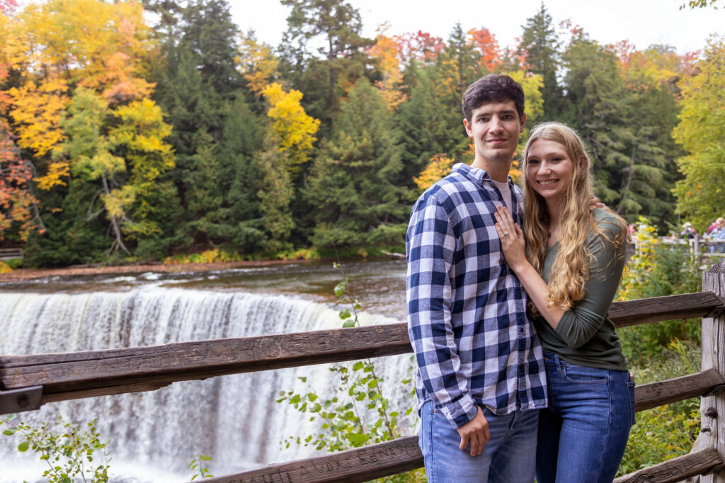 Newly engaged couple stands in front of Tahquamenon Falls in Paradise, Michigan.