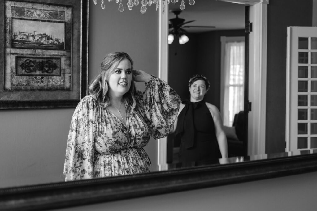 Nikki fixes her hair in the mirror at the Ishpeming AirBNB as Jillian looks on.