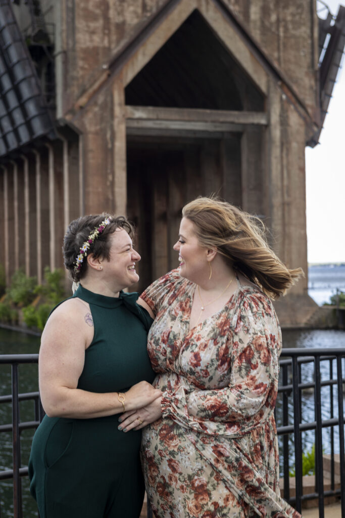 Same sex Michigan wedding couple smiles at each other in front of the Ore Dock in Marquette.