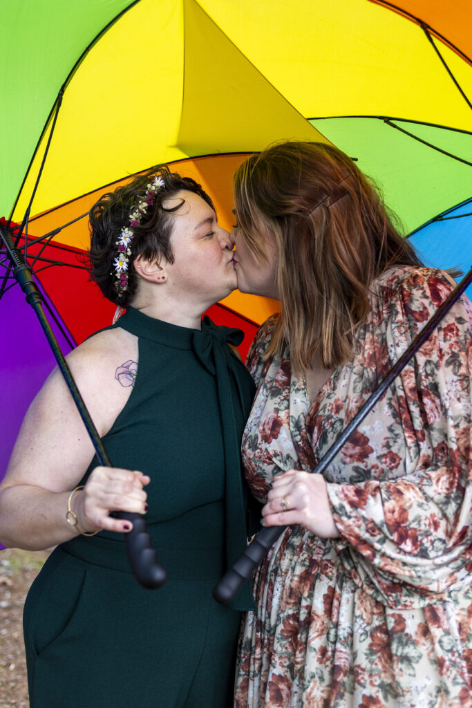 LGBT wedding couple poses under rainbow umbrellas during their Marquette, Michigan wedding.