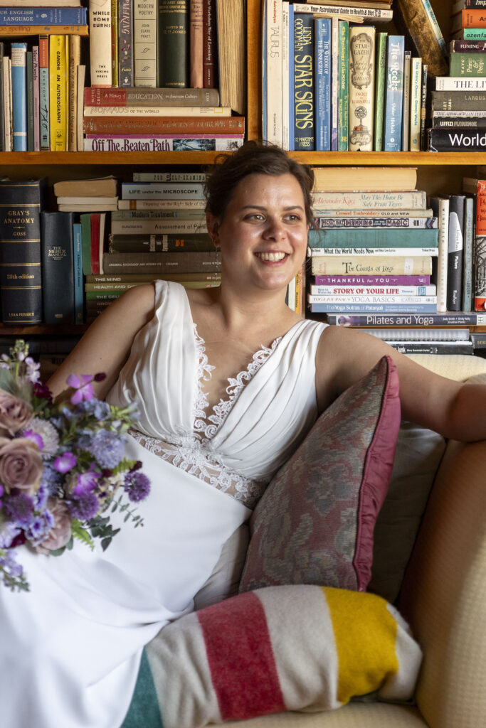 Bride smiling on chaise lounge in front of a wall of books at Pinecrest Northwoods