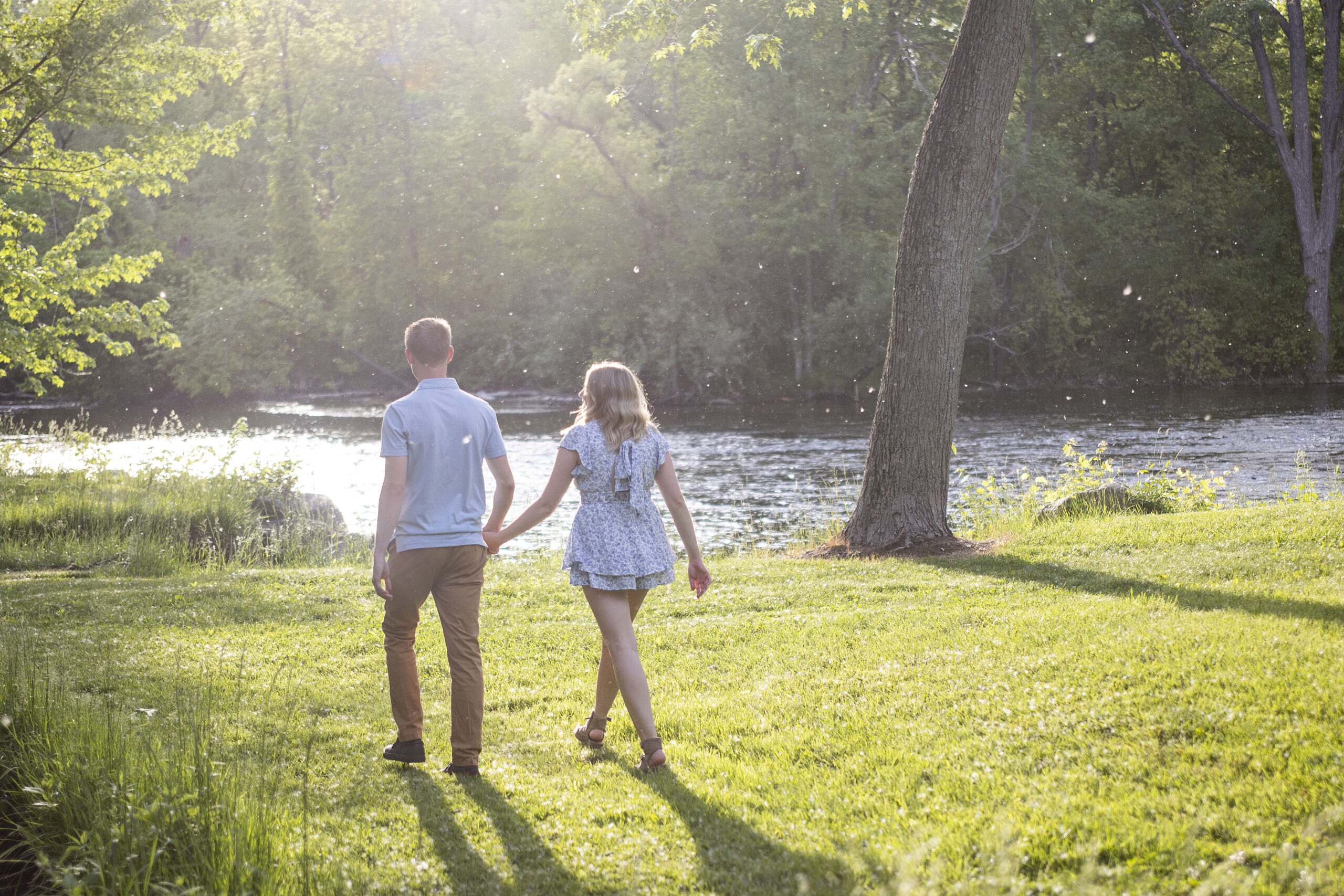 Tips for staying cool during your photo session - Couple walking under tree canopy with sunlight peeking through branches during summer photo session