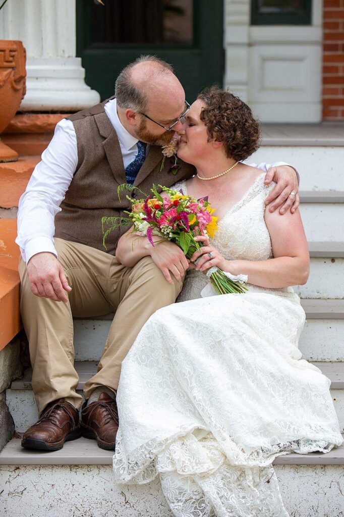 Sitting couple kisses on the steps of their Turner Dodge House wedding