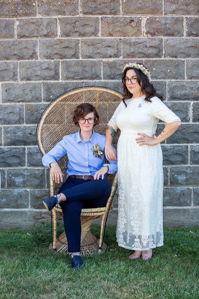 Queer wedding photographer poses couple in peacock chair