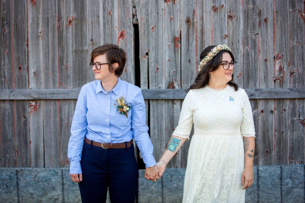 Queer friendly wedding photographer takes photos of lesbian couple in front of vintage barn.