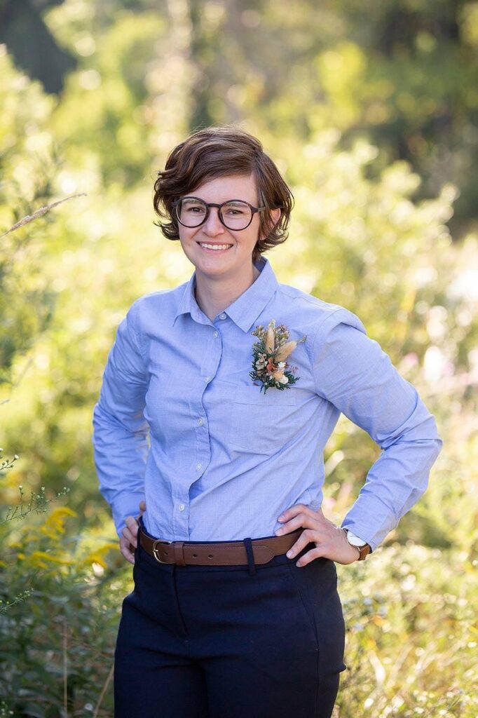 Queer bride poses in front of tall grass