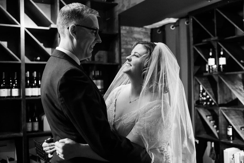 Bride and groom smile at each other while hugging at Vinology wedding