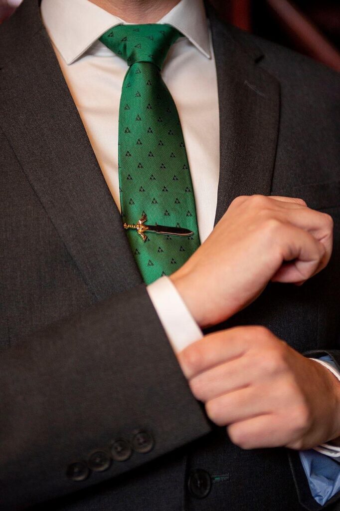 Groom fixing cufflink, Master Force sword tie clip in the background