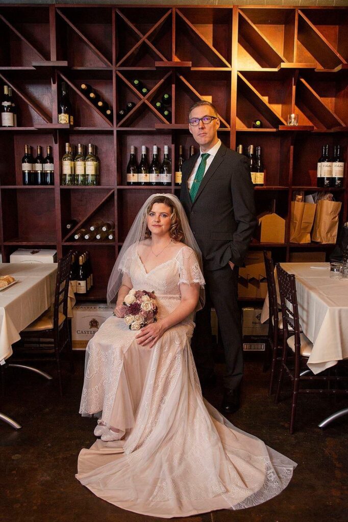 Bride sitting and groom standing in the wine cellar at Vinology in Ann Arbor