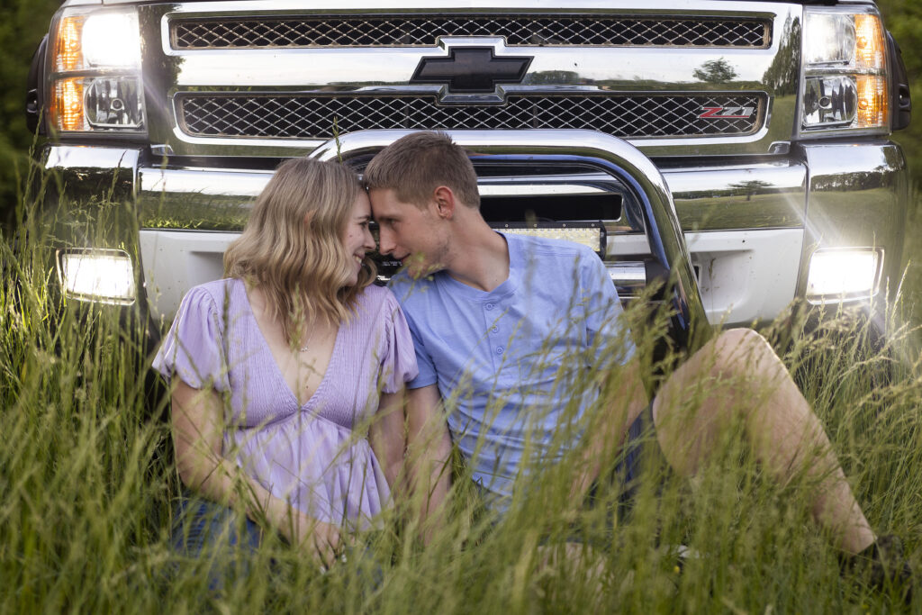 Talia leaning into Dakota as they sit in front of the truck, their foreheads touching sweetly