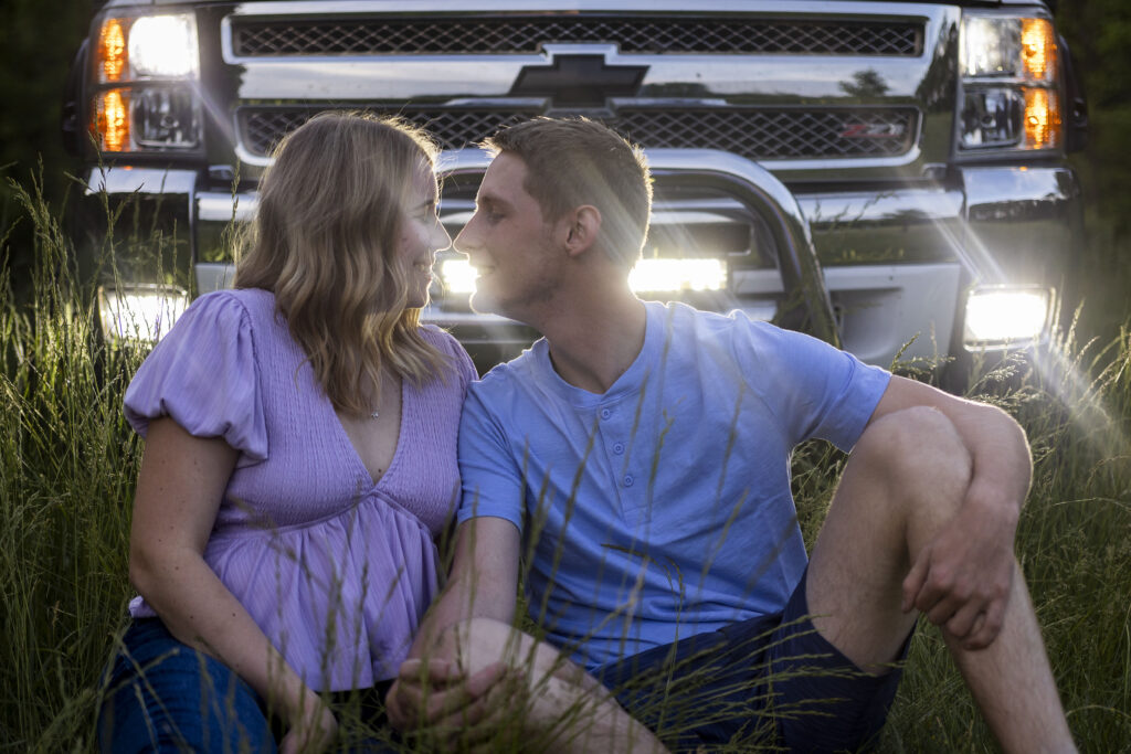 Couple kissing in front of the truck, surrounded by tall grass and headlights