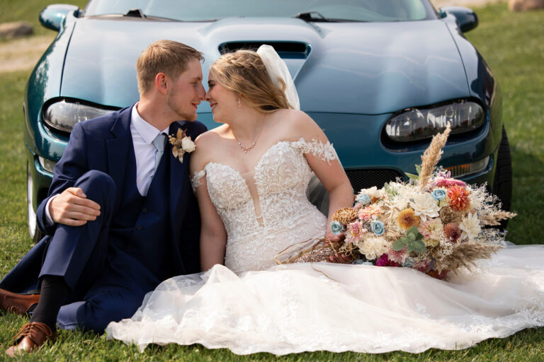 Bride and Groom sitting in front of his vintage Camaro