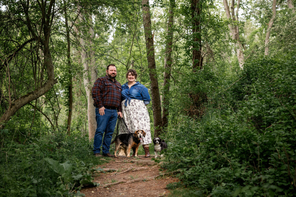 Couple walking with their two dogs through the woods at golden hour
