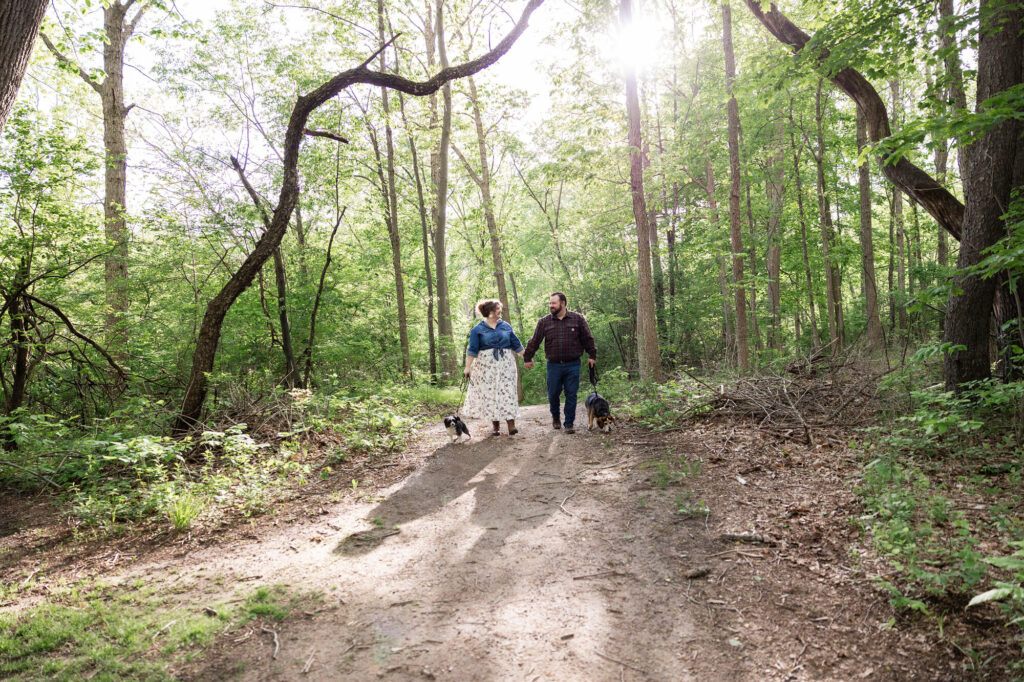 Natalie and Collin holding hands on a sunlit trail at Woldumar Nature Center