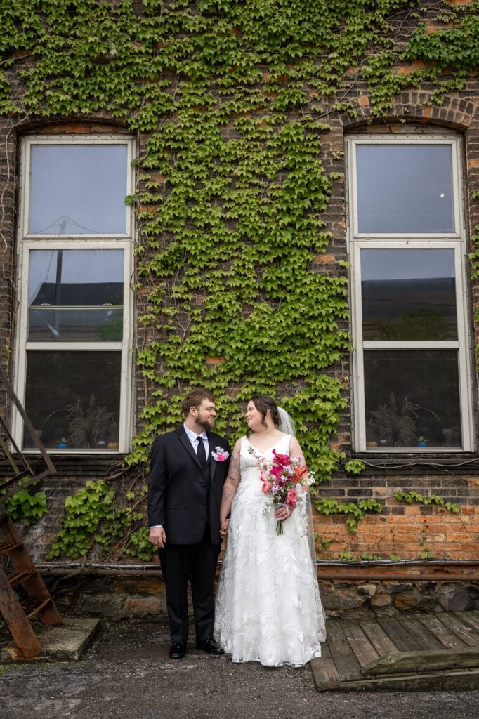 Art 634 wedding couple stands in front of a brick wall covered in ivy.